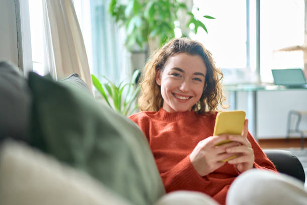 istock Smiling pretty young woman sitting on couch using mobile cell phone technology. 1455363661