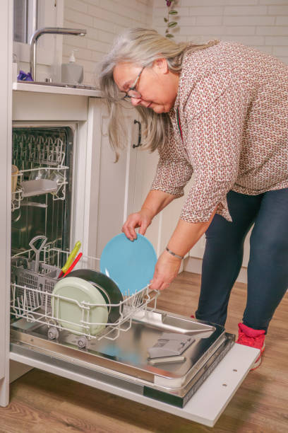 mulher colocando os pratos na máquina de lavar louça - home interior women domestic kitchen cabinet - fotografias e filmes do acervo