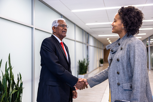 A senior black businessman and young businesswoman meet in the hallway