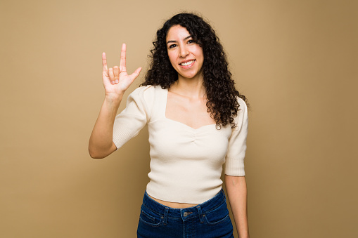 Happy attractive woman saying i love you using american sign language and smiling in front of a studio background