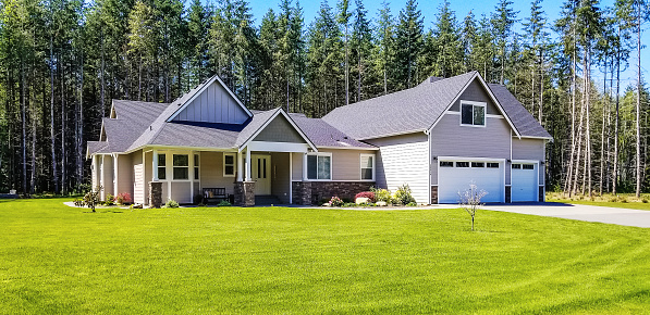 Photo of an upscale suburban home on a large lot, surrounded by forest trees on a bright summer day