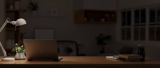 istock Dark workspace at night with laptop, stationery, table lamp, and decor on wood tabletop 1455383401
