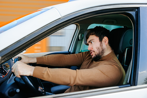 young bearded man at the wheel of a car with bizarre eccentric emotions. males with facially obvious emotions different funny, ridiculous idiotic