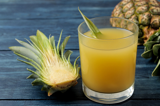 Pineapple juice in a glass and pieces of fresh pineapple on a blue wooden background. summer. fruits.