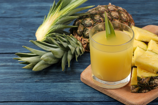 Pineapple juice in a glass and pieces of fresh pineapple on a blue wooden background. summer. fruits.