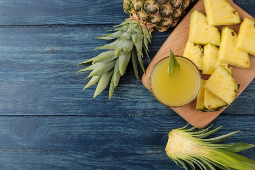 Pineapple juice in a glass and pieces of fresh pineapple on a blue wooden background. summer. fruits. top view
