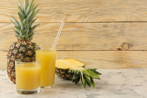 Pineapple juice in a glass and pieces of fresh pineapple on a natural wooden background. summer. fruits.