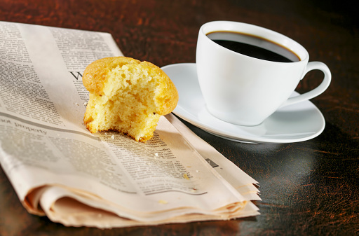 Vanilla muffin on top of a newspaper with coffee