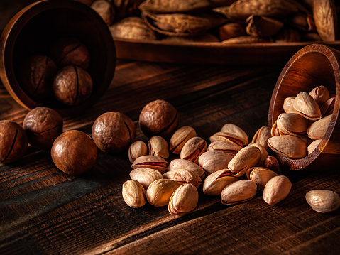 A handful of macadamia nuts and pistachios on a dark brown wooden background. Almonds in the shell in the background. Selective focus. Low key. Advertising poster. Art. Brown and coffee tones. Horizontal