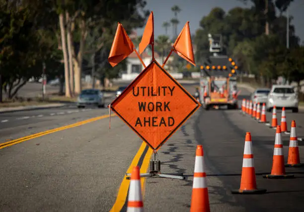 Photo of Traffic sign with flags reading Utility Work Ahead with traffic cones on road with electronic arrow pointing to the right to divert traffic