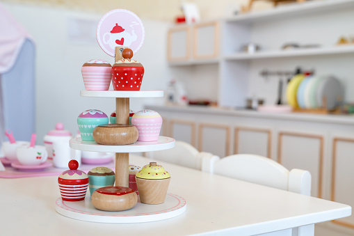 Enjoying an English afternoon tea TOY set made from wood with colorful cupcakes in a modern tower dish in a playground kitchen.