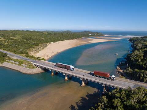 Aerial shot of two Transport trucks crossing the Kariega River in the Eastern Cape, South Africa. Transport trucks travelling along a scenic highway.