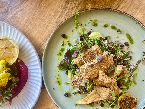 Horizontal flatlay of fresh salt and pepper squid seafood lunch with pesto, micro greens on bed of organic  quinoa salad ceramic plates on wood table near Coffs Harbour NSW Australia