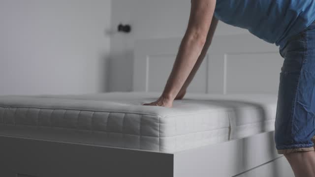 The man bought a new mattress for his bedroom. The owner puts the mattress on the bed and checks its quality