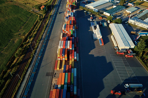 Shipping containers in terminal, Unloading containers in warehouse on railroad platform with cranes and forklifts, aerial view