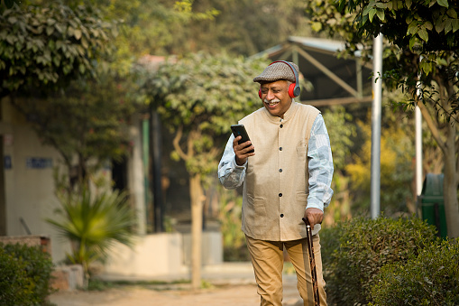 Senior man with walking cane listening music on headphones at park
