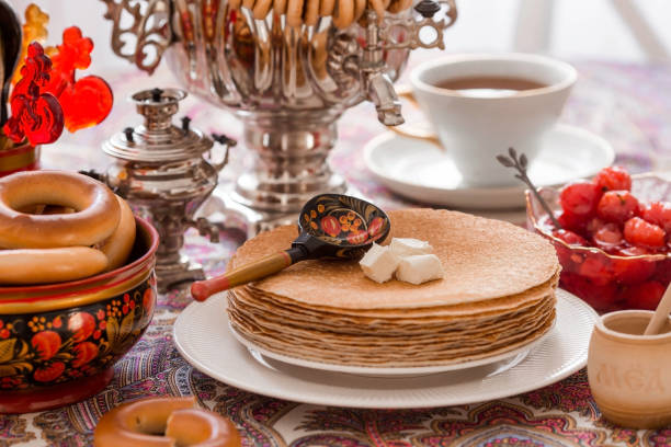 istock Russian traditions. Russian holiday Maslenitsa. Still life with a cup of tea, a stack of pancakes, sour cream, honey, cubes of butter, bagels, dried fruits, caramel cockerel and samovars. 1455412593
