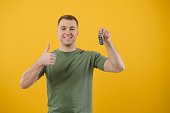 Shocked young man posing isolated on yellow orange background, studio portrait. People emotions lifestyle concept. Mock up copy space. Holding in hand car keys, showing thumb up