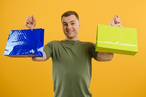 portrait of smiling couple holding shopping bags isolated on yellow background.