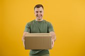 Cute man holding a cardboard box on a yellow background. Delivery service concept. Free space for advertising.