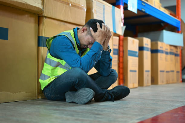 istock Tired warehouse worker taking break from hard work, sitting between rows full of shelves with goods in cardboard boxes. 1455416164