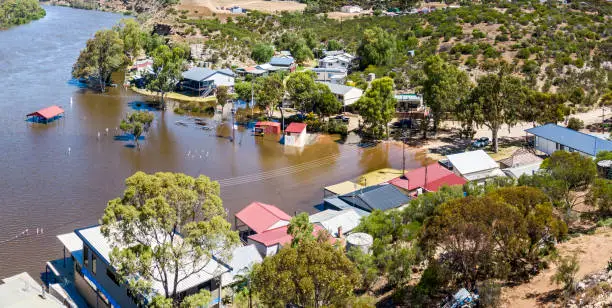 Aerial panoramic view of small River Murray community of Caloote threatened by rising floodwaters. The picnic area is underwater with facilities submerged, public toilets and some properties under threat. The normally popular public park area is a bay of muddy floodwater from the rapidly flowing river in the background. Dec 17, 2022.