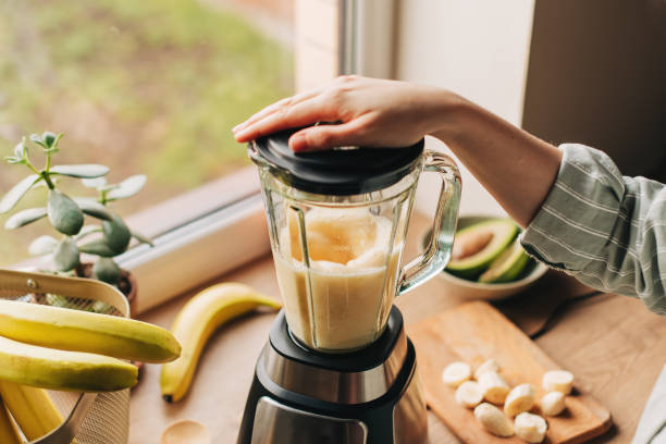 frau, die spinat, beeren, bananen und mandelmilch mischt, um einen gesunden grünen smoothie herzustellen - superfood stock-fotos und bilder