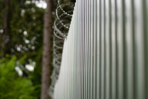 Steel fence with barbed wire. Fence around plant. Private territory. Metal profile. Dangerous wire. Steel fence with barbed wire. Fence around plant. Private territory. Metal profile. Dangerous wire. High barrier. barbed wire wire factory sky stock pictures, royalty-free photos & images
