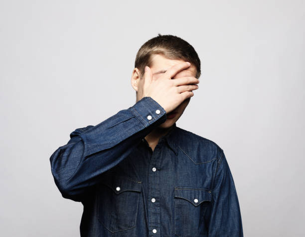 istock A young handsome man covers his eyes with his palm over grey background. 1455418533