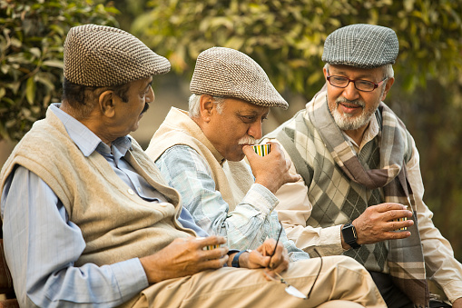 Happy senior male friends drinking tea while relaxing on park bench