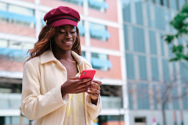 istock Woman smiling while using a mobile phone walking outdoors on the street. 1455423697