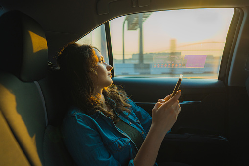 Young Caucasian woman with smartphone on backseat of taxi in Dubai at sunset