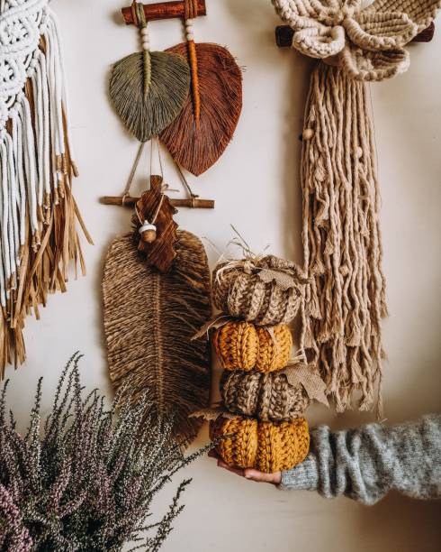 istock Woman holding macrame pumpkins with macrame feathers hanging on a white wall in the background 1455431933