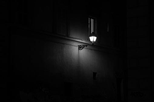 A dark view of a street lamp on a wall of a building with small window
