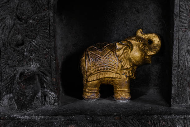 istock Small golden Indian elephant statue positioned in a dark black wall 1455437744