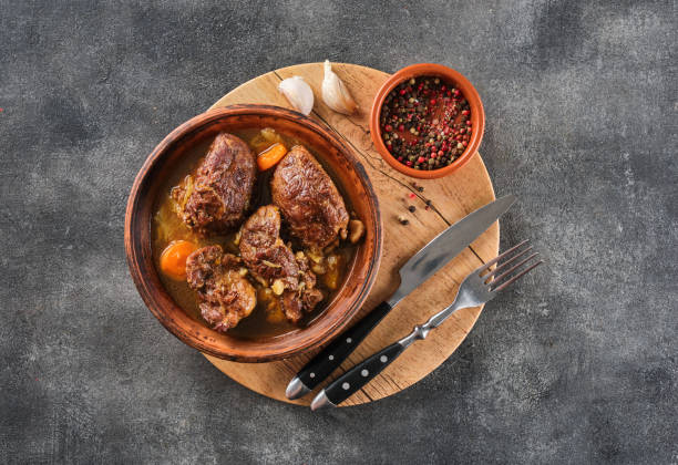 istock Stewed pork cheeks with vegetables on wooden board with pepper and garlic. Top view. 1455438193