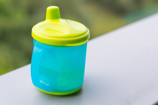 A closeup shot of green and blue plastic baby drinking cup on a white surface