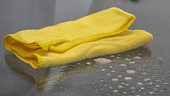 Closeup shot of a yellow microfiber cloth on a glass table with a spray