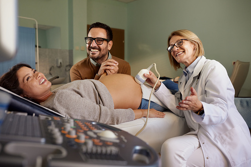 Happy man holding hands with his pregnant wife during an ultrasound at gynecologists'.