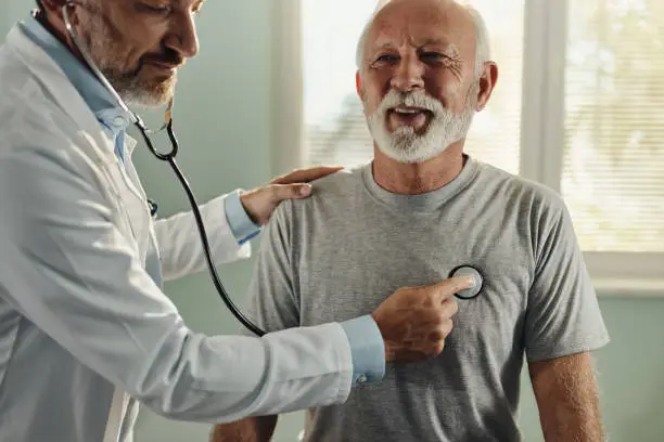 Mid adult male doctor listening to senior man's heartbeat during an appointment in the office.