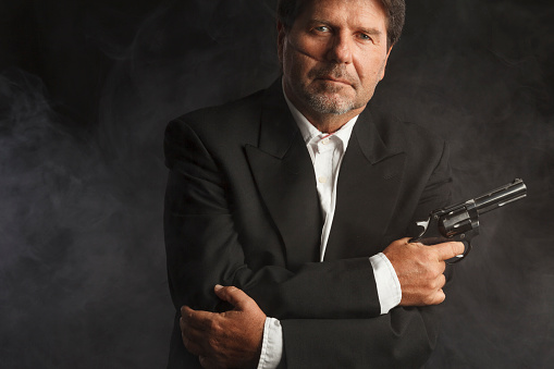 Scar face. Vintage portrait of a senior man in black suit,  holding a gun. Cold and dangerous expression, deep look into camera.
