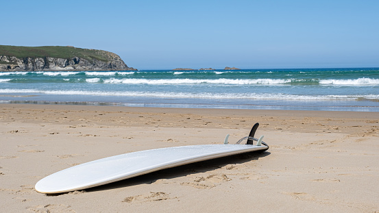 A shot of a surf board on a beach in the background of a wavysea.