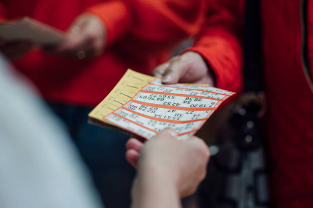An unrecognisable woman passing a bingo card to another unrecognisable woman who has just paid to play bingo.
