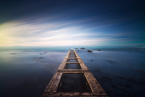 Wooden pier or jetty remains in a blue sea at sunrise. Livorno, Tuscany region. Long Exposure photograph.