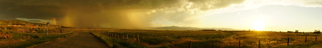 A panoramic view of a trail in a green fenced field in Montana during a thunderstorm