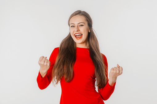 Excited young woman winning, triumphing, screaming with joy and fist pump, feeling relieved, achieve success, standing over white background