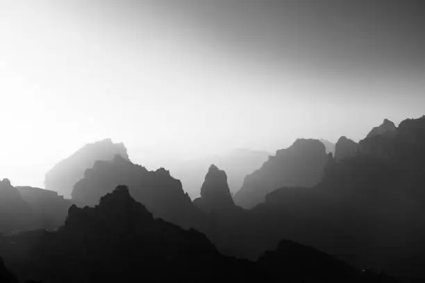 Photo of Aerial view of rocky mountains on a foggy day shot in grayscale