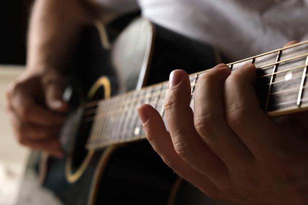 playing the guitar. strumming acoustic guitar. musician plays music. man fingers holding mediator. man hand playing guitar neck in dark room. unrecognizable person rehearsing, fretboard close-up. - jam up imagens e fotografias de stock