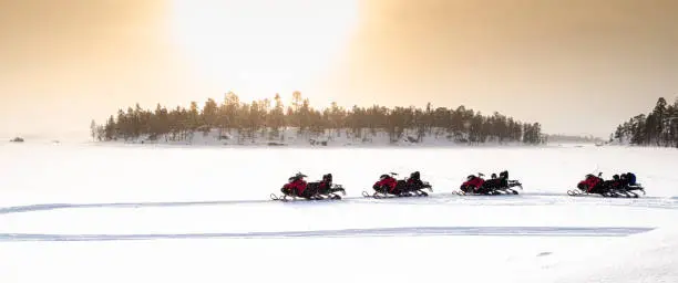 Panoramic landscape with a row of 4 red snowmobiles parked in the snow during adventure day on frozen Lake Inari, Finland, Lapland. Sunrise moment in winter season. No people.
