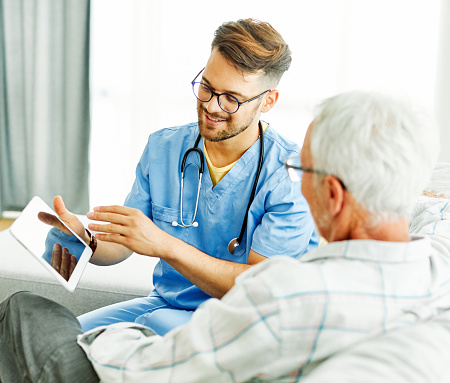 Doctor or nurse caregiver showing a tablet screen to  senior man at home or nursing home